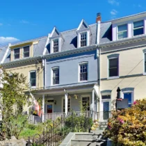 Front exterior of a painted 1910 Petworth row house with a mansard roof, dormer windows and a covered front porch at 4213 8th St NW, Washington DC