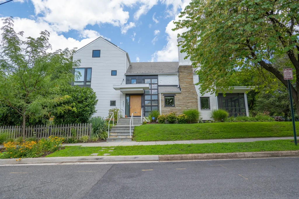 Contemporary renovated home with white siding, a stone chimney and a wood front door in American University Park, Washington, DC