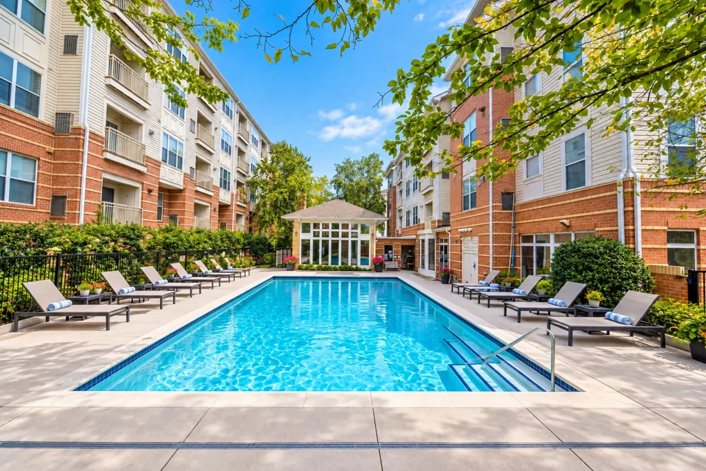 Outdoor pool with lounge chairs and a glass-walled pool pavilion between four-story condominium buildings in Virginia Center, Vienna VA